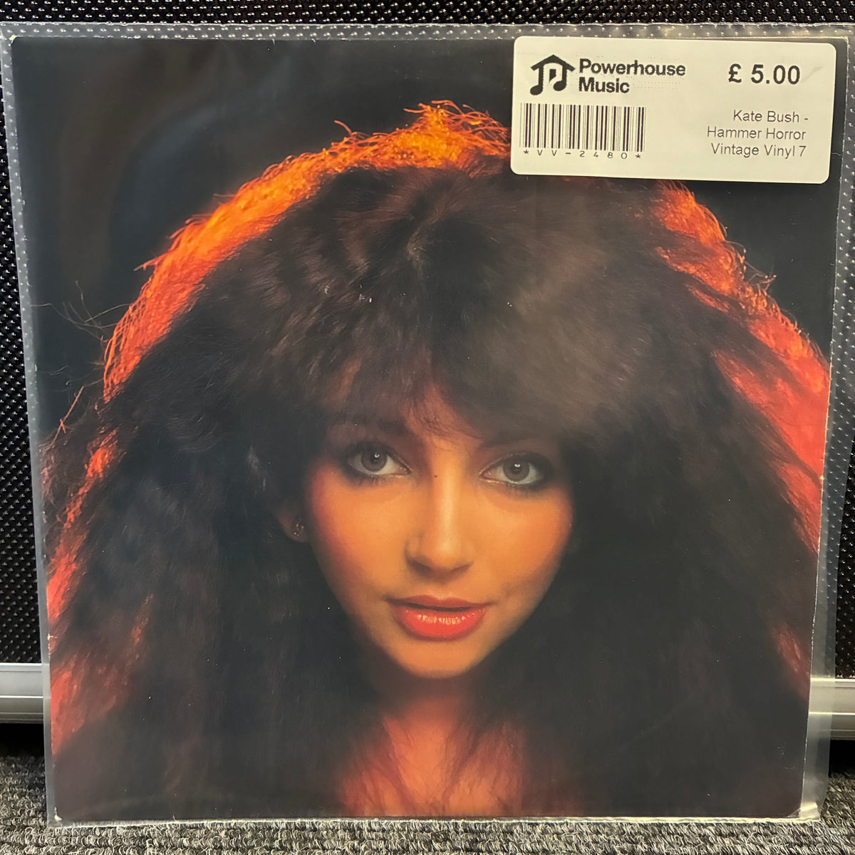Kate Bush - Hammer Horror Vintage Vinyl 7" Single A vintage vinyl record sleeve for Kate Bush's 'Hammer Honor' on Powerhouse Music, featuring a close-up portrait of the artist with voluminous dark hair and a bright orange glow. A white barcode sticker showing the price of £5.