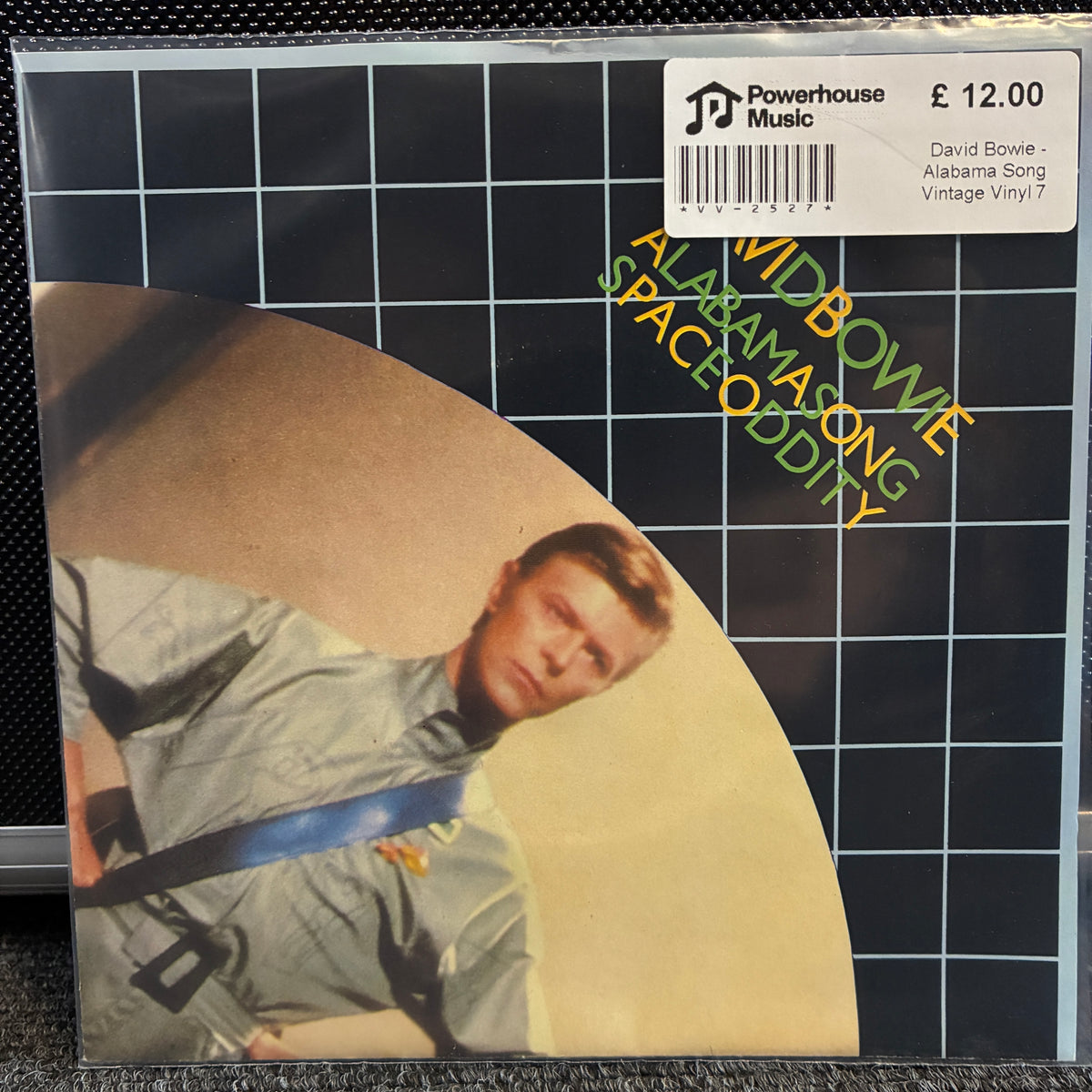 David Bowie - Alabama Song Vintage Vinyl 7" Single A sealed vinyl record sleeve of David Bowie's 'Aladdin Sane - Space Oddity' on Powerhouse Music, featuring the album art with a black grid background, a beige circular shape, and a photo of Bowie in a gray uniform. A white barcode sticker with pricing is visible in the top right.