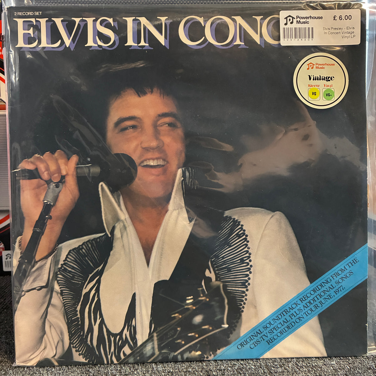 Elvis Presley - Elvis In Concert Vintage Vinyl LP Elvis In Concert vinyl record album cover, showing Elvis Presley holding a microphone and wearing a white shirt with black patterned lapels. The record sleeve has a visible 'Vintage' sticker and a barcode price label in the top right, and the title 'ELVIS IN CONCERT' across the top.