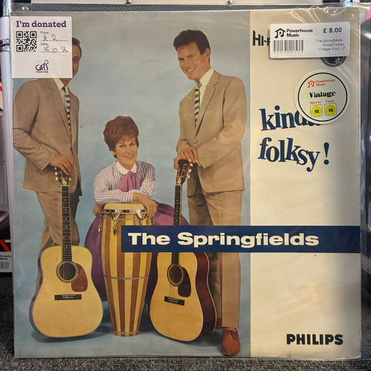 The Springfields - Kinda Folksy Vintage Vinyl LP The Springfield 'Kind of Folksy!' vinyl record album cover on a record store shelf. The cover features the band members in tan suits with acoustic and conga guitars, set against a light blue background with a white right-hand panel containing the title and Philips branding.
