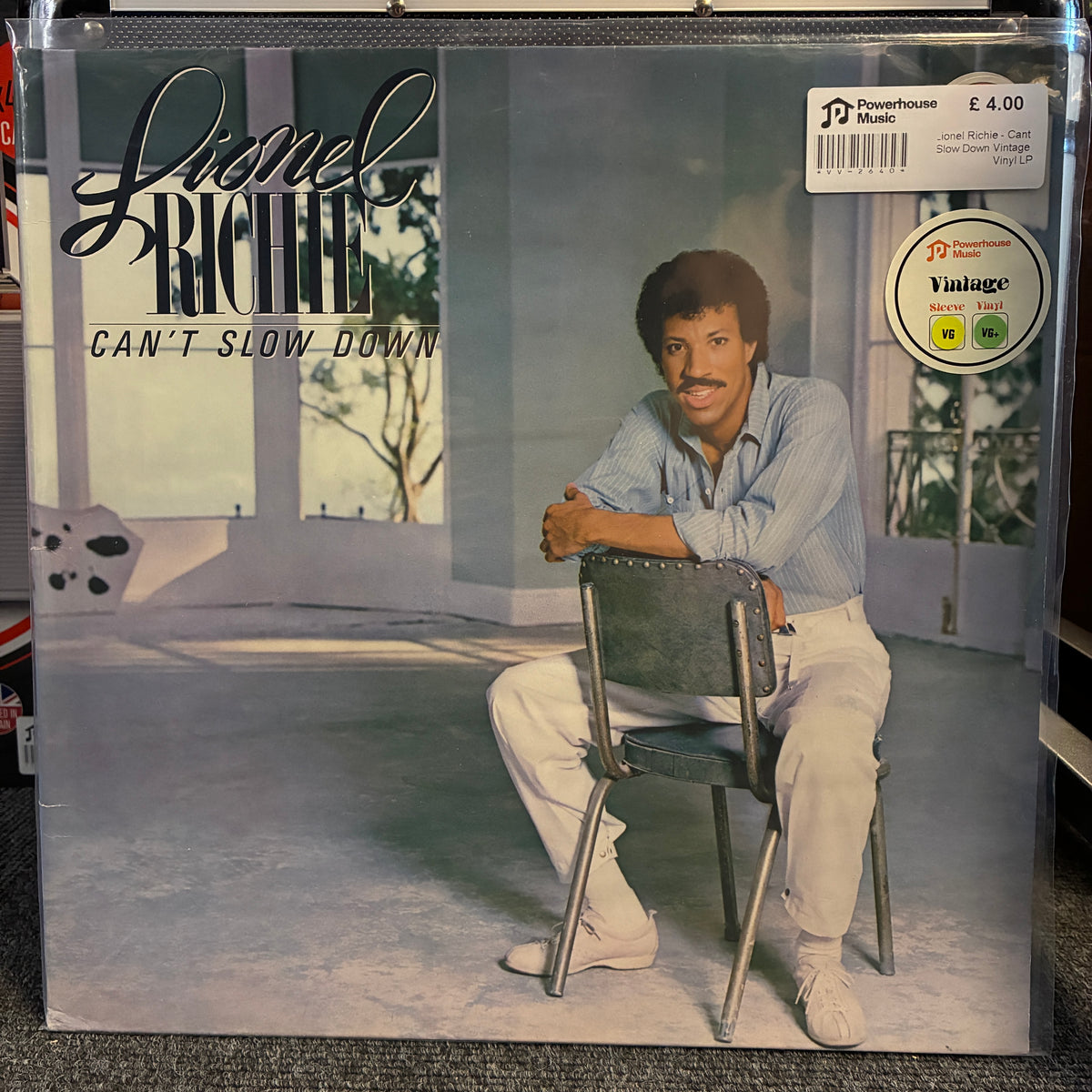 Lionel Richie - Can't Slow Down Vintage Vinyl LP Lionel Richie 'Can't Slow Down' vinyl record album cover, showing Lionel Richie seated on a chair in a modern interior. The cover has a Powerhouse label sticker and a Vintaglia sticker on the top right, photographed inside a clear plastic sleeve.