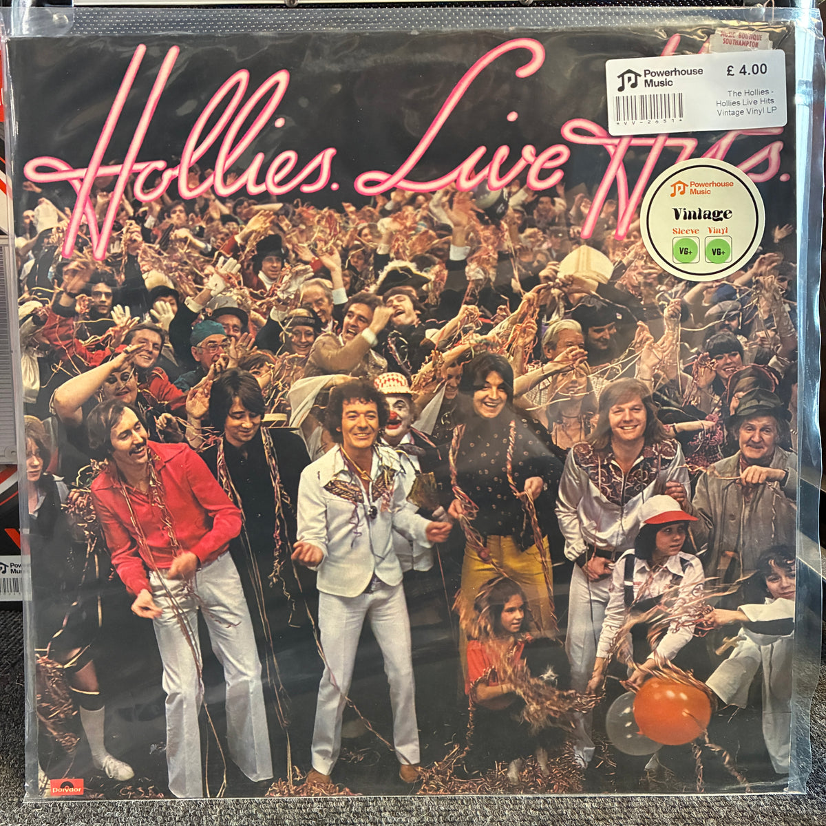 The Hollies - Hollies Live Hits Vintage Vinyl LP Hollies 'Live 70' vinyl record album cover in clear plastic shrink-wrap, with a barcode sticker and a round 'Vintage' label on the front. The cover shows a large crowd scene with the band members in colorful clothing, and the title 'Hollies Live 70' in pink script across the top.