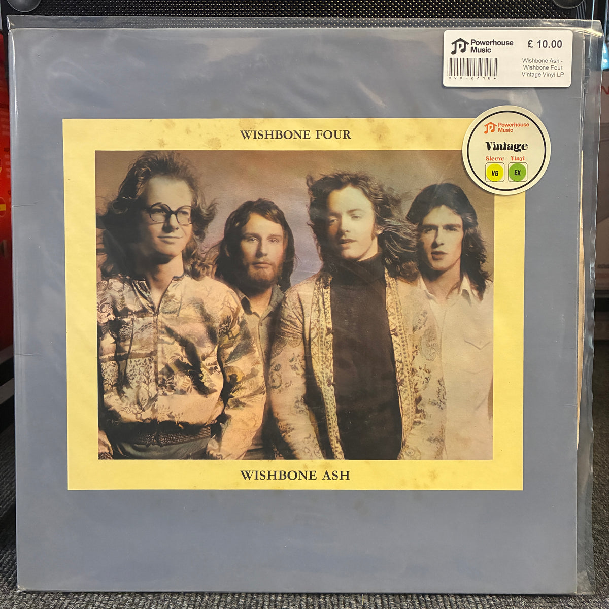 Wishbone Ash - Wishbone Four Vintage Vinyl LP A vinyl record sleeve for the band Wishbone Four, featuring a vintage-style portrait of four men on a yellow background, photographed inside a clear plastic protective case. A Powerhouse Music sticker is visible in the top right corner.