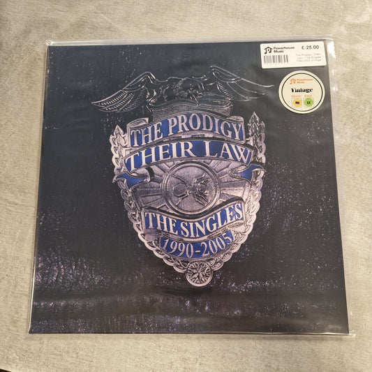 The Prodigy - Their Law - The Singles 1990-2005 Vintage Vinyl LP The Prodigy 'Their Law - The Singles 1990-1991' vinyl record album in its clear plastic shrink-wrap, resting on a textured gray surface. The cover art features a silver-toned police badge with blue lettering.