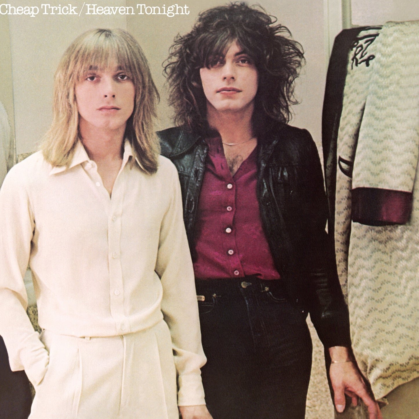 Cheap Trick - Heaven Tonight (Translucent Violet) Vinyl Two men standing indoors, one with long blonde hair wearing a cream button-up shirt and matching pants, and the other with dark curly hair wearing a black leather jacket over a burgundy button-up shirt and dark pants. A patterned garment hangs on a rack to the right, and the text 'Cheap Trick / Heaven Tonight' appears at the top.