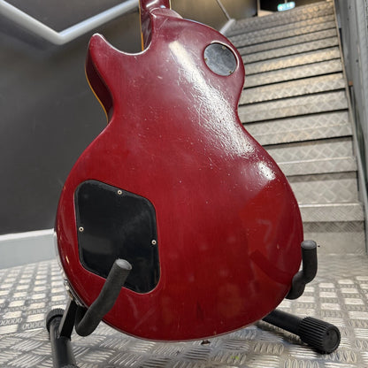 Pre-Owned Gibson Les Paul Classic '1960' 2001 Electric - Cherry Sunburst A red electric guitar body, likely a Gibson Les Paul style, shown from the back on a black stand in front of a metal staircase.