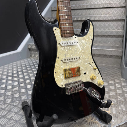 Pre-Owned Fender USA American Traditional Fat Stratocaster (Export Model) 1999 Electric - Black A black electric guitar with a cream-colored pickguard and gold hardware, resting on a stand on a diamond plate floor.