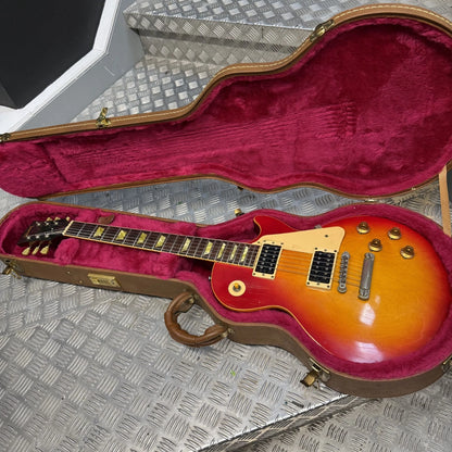 Pre-Owned Gibson Les Paul Classic '1960' 2001 Electric - Cherry Sunburst An open Gibson electric guitar case with a brown hard shell and deep magenta velvet lining, containing a sunburst electric guitar on a diamond plate metal surface.