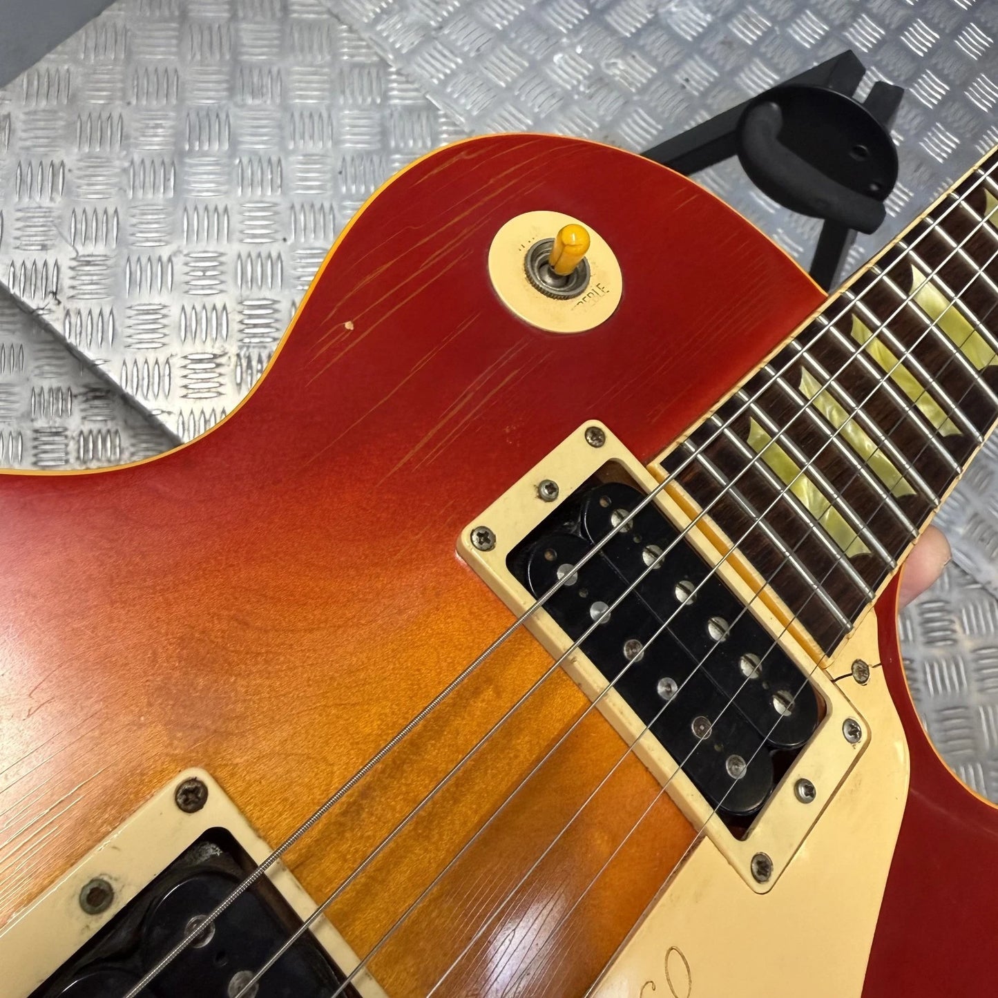 Pre-Owned Gibson Les Paul Classic '1960' 2001 Electric - Cherry Sunburst Close-up of a sunburst electric guitar body with cream-colored pickups and a black humbucker pickup, resting on a silver diamond plate background.