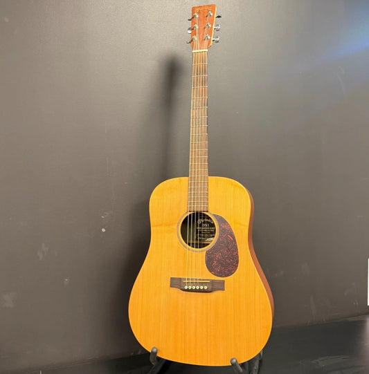 Pre-Owned Martin DX1 Acoustic guitar on a stand against a dark wall