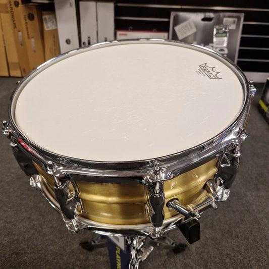 Pre-Owned Yamaha RRS1455 Snare drum with gold body and white head on a stand in a store setting