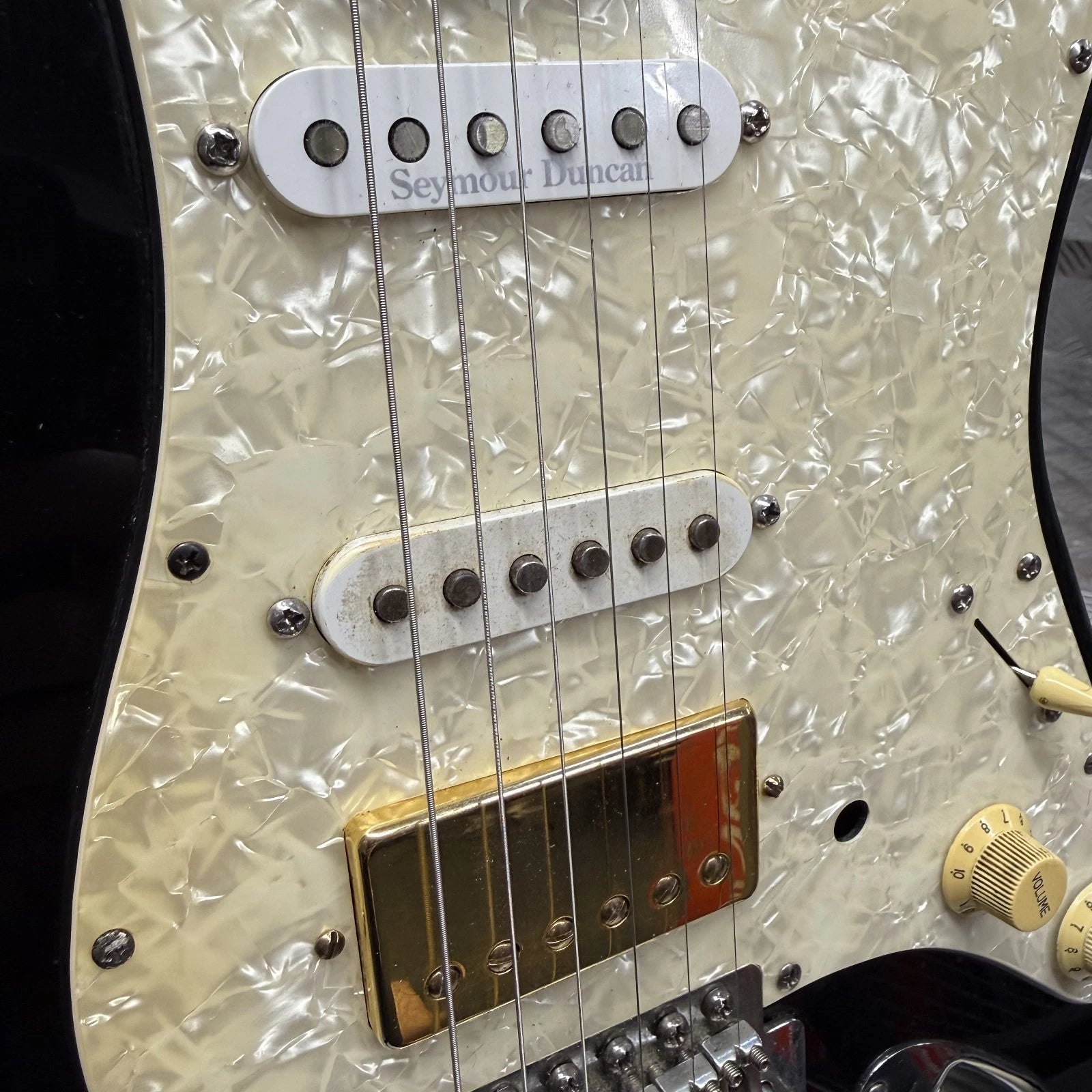 Pre-Owned Fender USA American Traditional Fat Stratocaster (Export Model) 1999 Electric - Black Close-up of a guitar body featuring a cream pearlescent shell pattern, white Seymour Duncan humbucker pickups, a gold-toned bridge plate, and black edge binding.