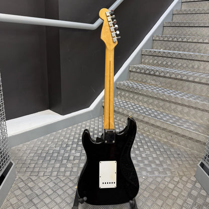 Pre-Owned Fender USA American Traditional Fat Stratocaster (Export Model) 1999 Electric - Black A black electric guitar with a natural wood neck, standing on a stand on a diamond-plate metal staircase in an industrial setting.