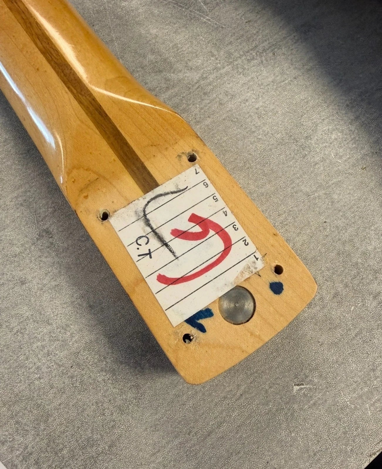 Pre-Owned Fender USA American Traditional Fat Stratocaster (Export Model) 1999 Electric - Black Close-up of a light natural wood guitar headstock corner with a white measurement tape measure sticker marked with red and black markings, placed on a gray textured surface.