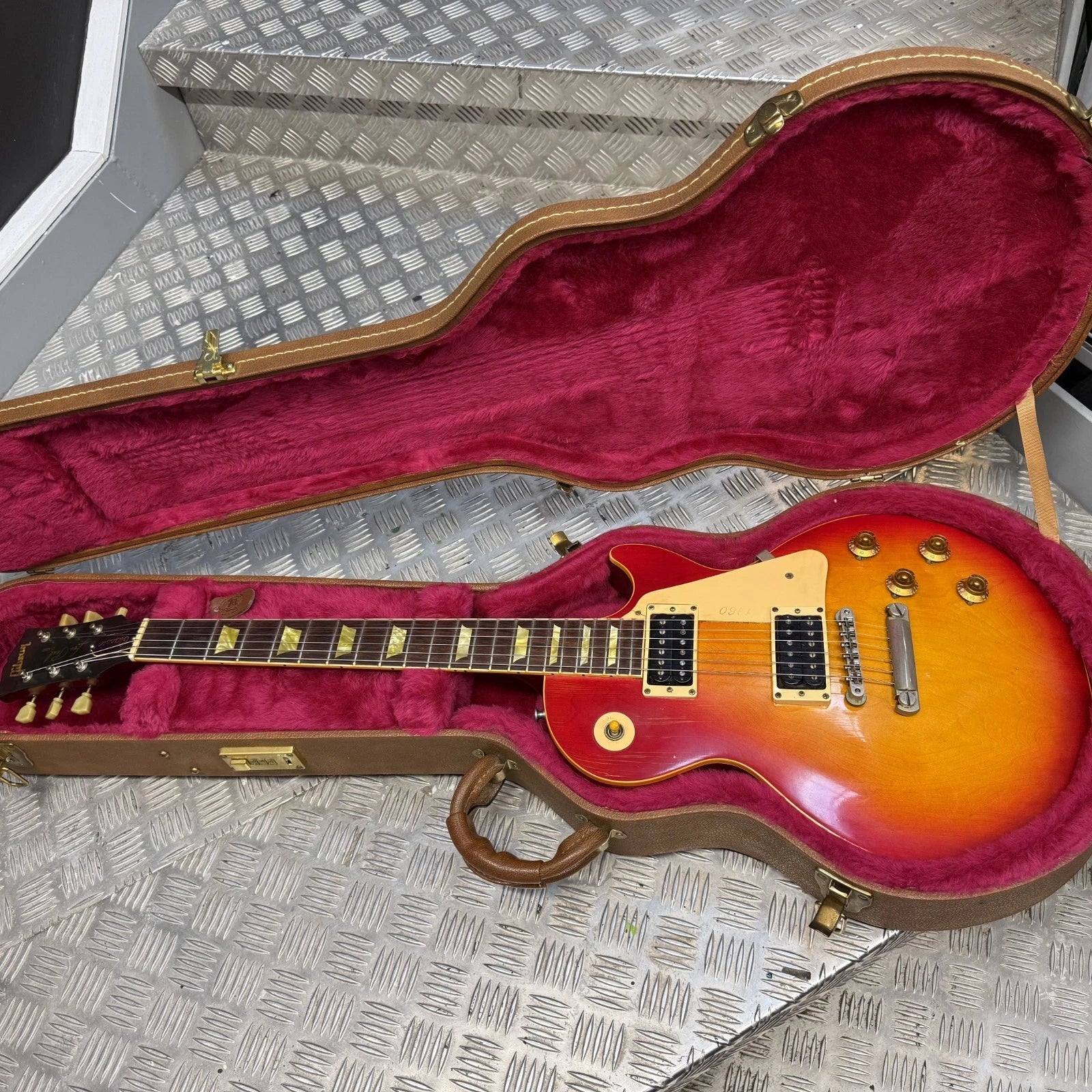 Pre-Owned Gibson Les Paul Classic '1960' 2001 Electric - Cherry Sunburst A Les Paul style electric guitar with a sunburst finish, displayed inside an open hard case with a magenta velvet interior on a diamond plate metal surface.