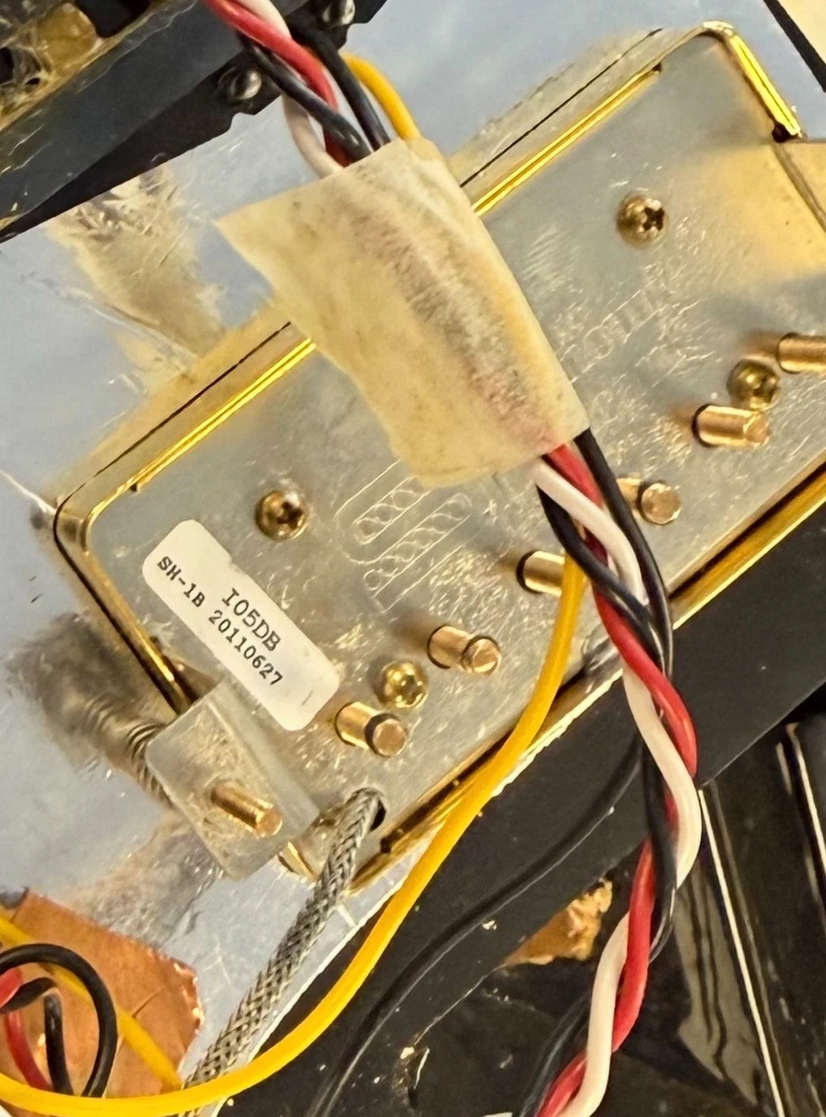 Pre-Owned Fender USA American Traditional Fat Stratocaster (Export Model) 1999 Electric - Black A close-up of an electronic control module with a brushed metal casing, gold-colored terminal screws, attached wiring in red, white, and black, and a beige tape wrap around the connector area.