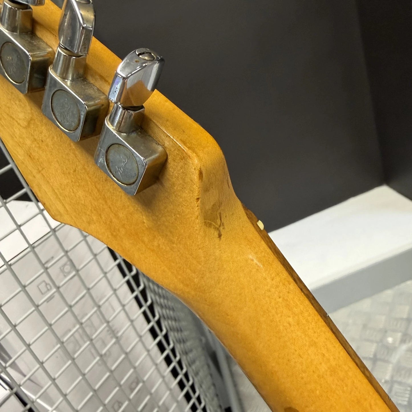 Pre-Owned Fender USA American Traditional Fat Stratocaster (Export Model) 1999 Electric - Black Close-up of the headstock of an electric guitar, showing a yellow-orange maple wood neck with four silver metal tuning pegs against a dark gray background.