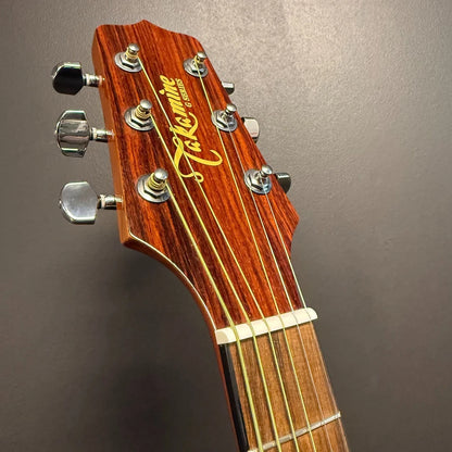 Pre-Owned Takamine EG530SC Close-up of a Takamine guitar headstock on a grey background