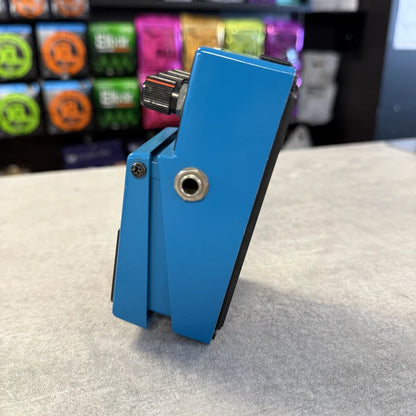 Pre-Owned Boss VB-2 Blue guitar pedal on a gray surface with colorful boxes in the background
