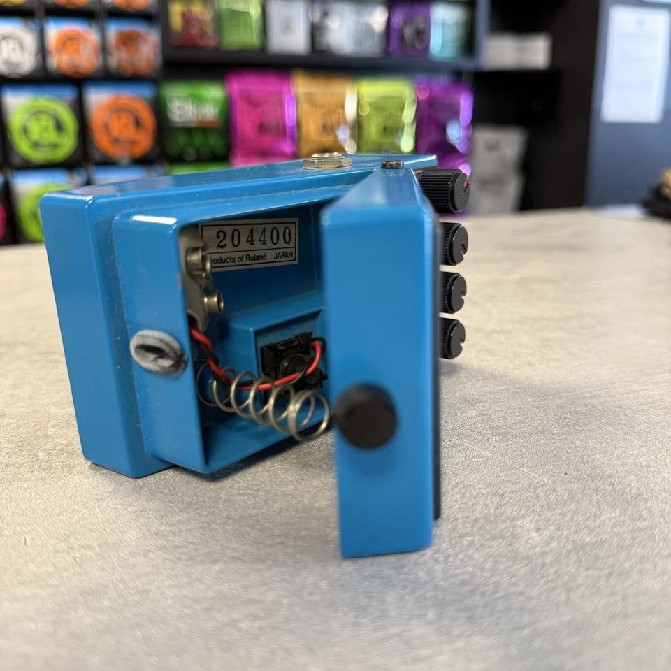 Pre-Owned Boss VB-2 Blue electronic device with visible components on a light gray surface, with colorful boxes in the background.
