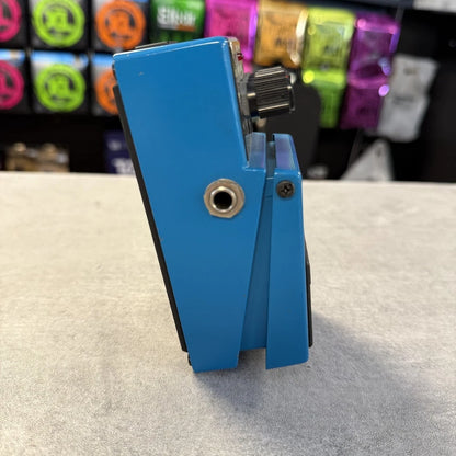 Pre-Owned Boss VB-2 Blue guitar pedal on a light gray surface with colorful boxes in the background